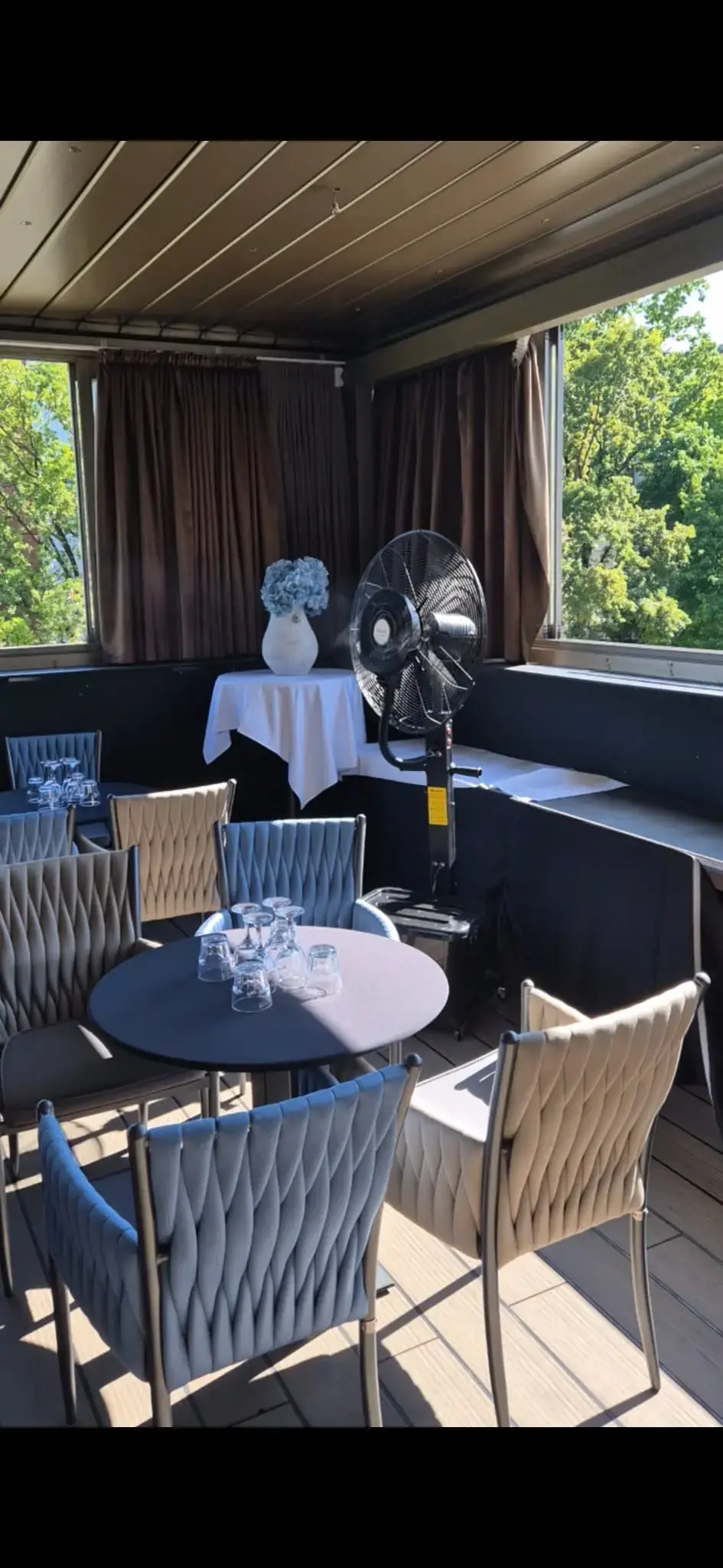 Elegantna zatvorena terasa restorana s ventilatorom na vodu pored stola s cvijećem